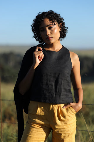 Woman wearing a black linen tank top and yellow linen pants standing in a field with a blurred background