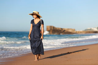 Woman in a navy linen dress and straw hat walking on a beach in Durban, South Africa, with ocean waves in the background