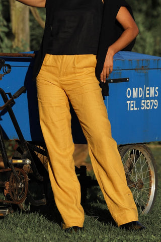 Lady wearing mustard yellow linen pants with a black linen top standing next to a blue cart.